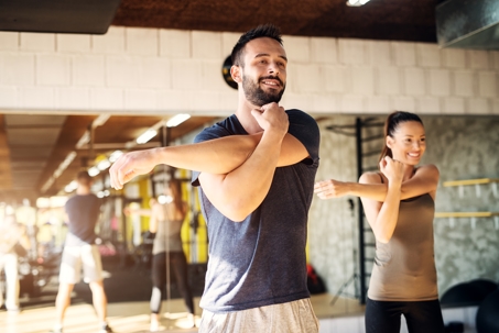 Man and woman smiling while stretching in gym.