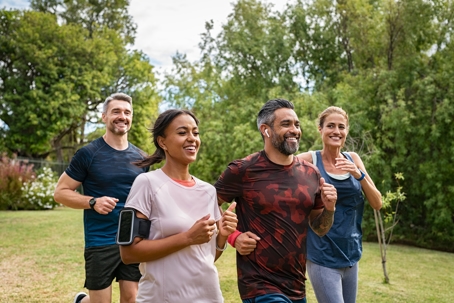 Group of people smiling while jogging through the park together.
