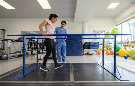 Woman walking on parallel bars with physical therapist.
