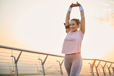 Woman stretching at sunrise before going on a run. She is living an active and healthy lifestyle, smiling as she starts the day with a workout. | ProFysio Physical Therapy