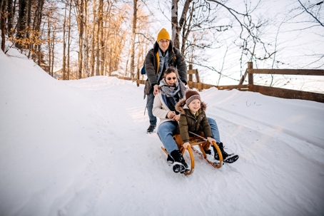 Family of three sledding down a hill on a snowy day. | ProFysio Physical Therapy
