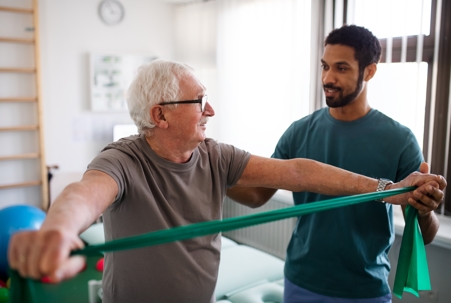 Physical therapist assisting elderly man with exercises.