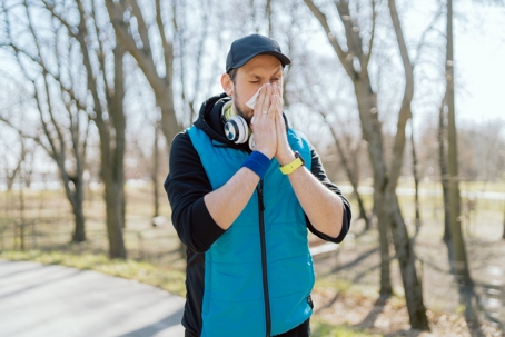 Man with seasonal allergies stopping to blow nose while jogging in the park.