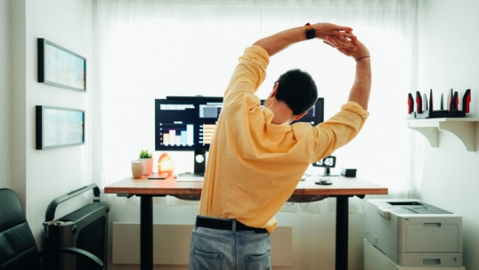 Man stretching at ergonomic workspace while working from home.