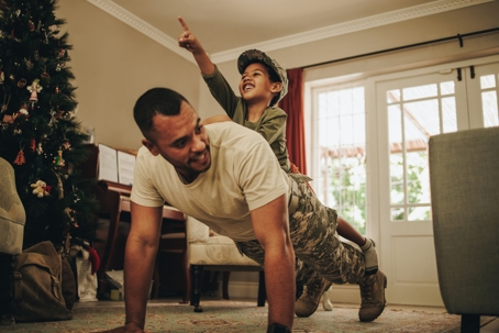 Father doing pushups in decorated holiday living room with his son on his back.
