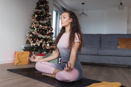 Woman doing yoga in her living room with decorated tree in background.