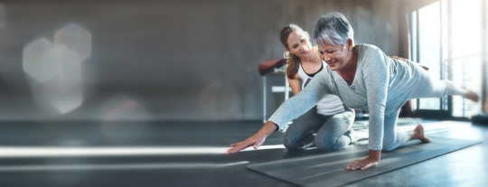 Older woman doing stretches and floor exercises with a physical therapist. They are smiling as the patient is achieving physical goals. | ProFysio Physical Therapy