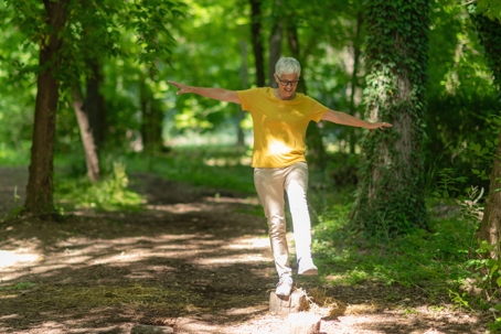 Older woman balancing on a small rock while walking along a wooded trail. | ProFysio Physical Therapy